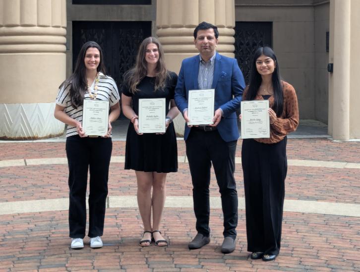 four event speakers standing outdoors holding certificates