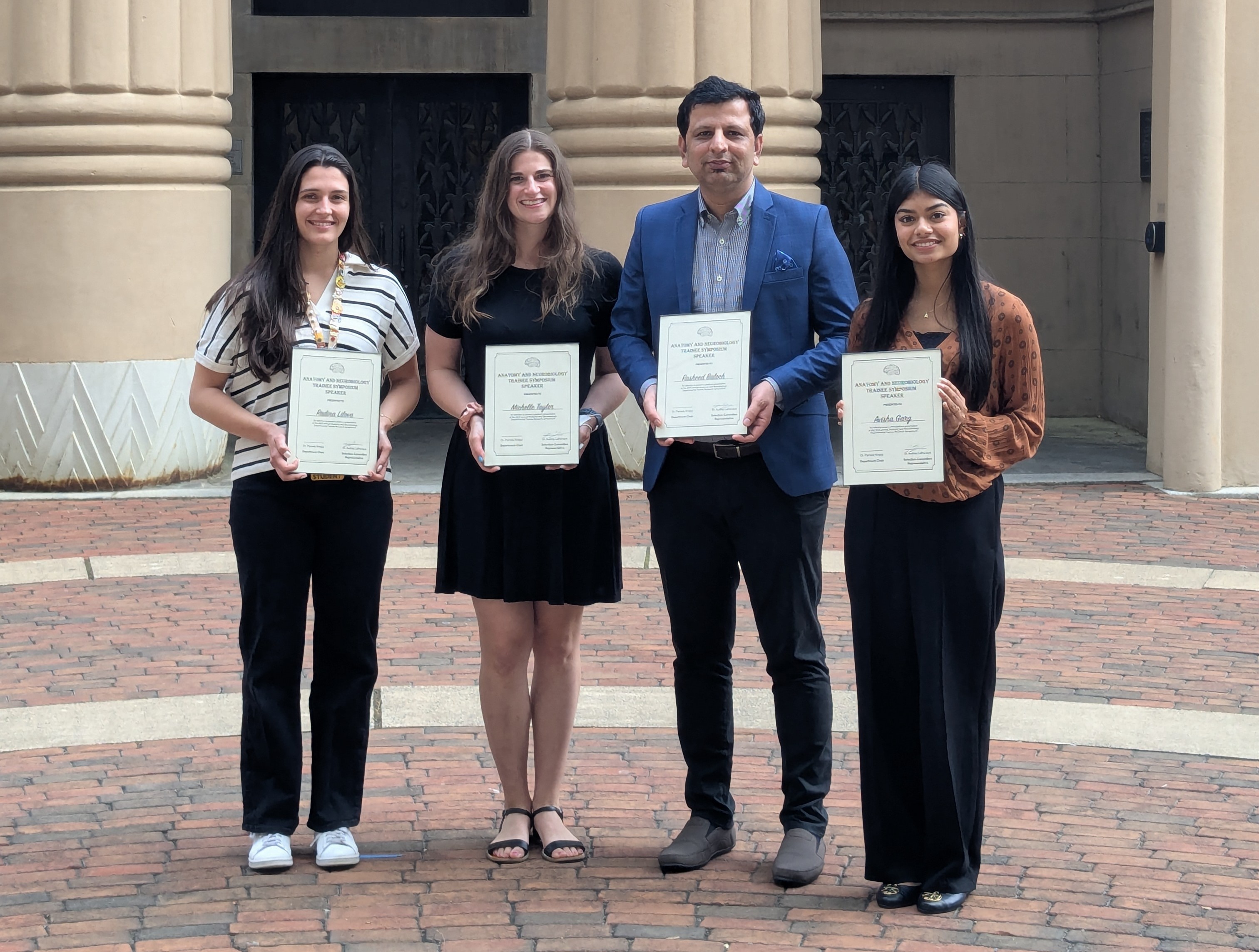four event speakers standing outdoors holding certificates